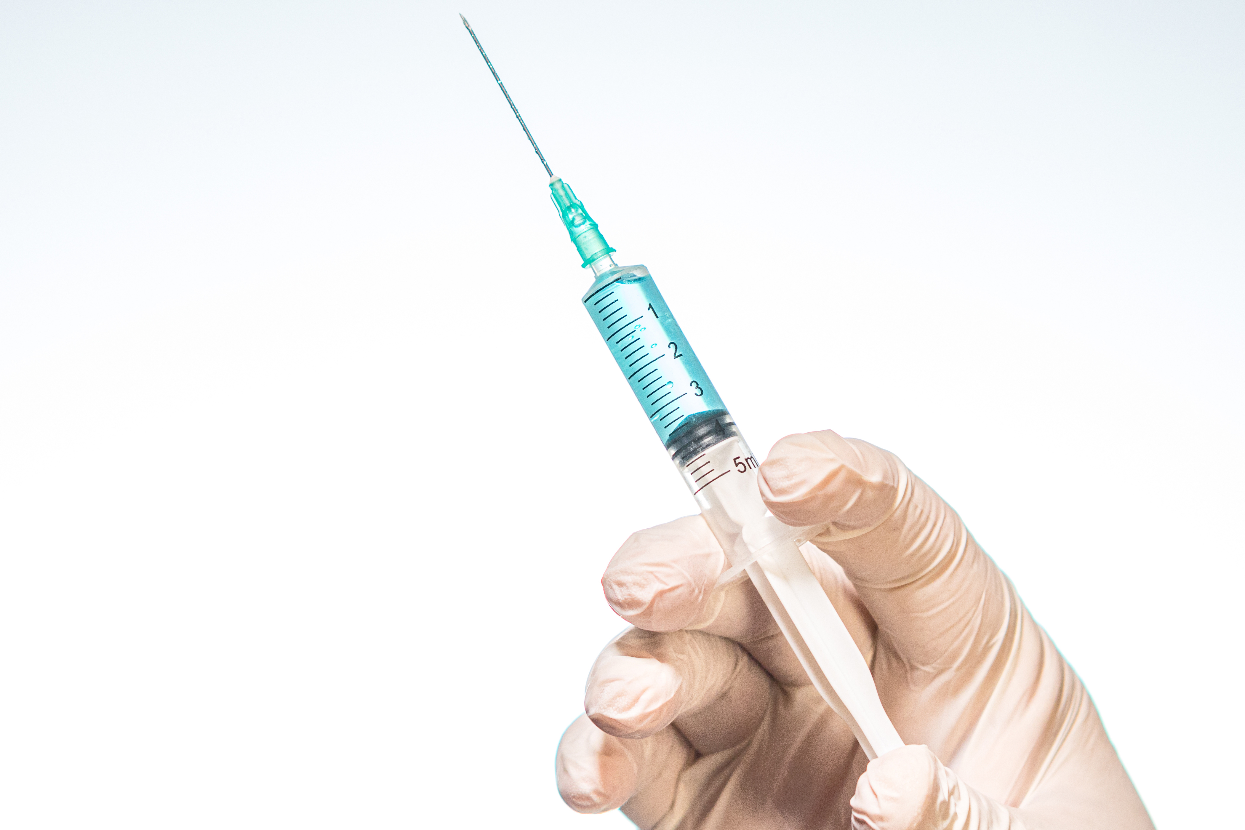 A person's hand wearing a surgical glove and holding a syringe with a white background